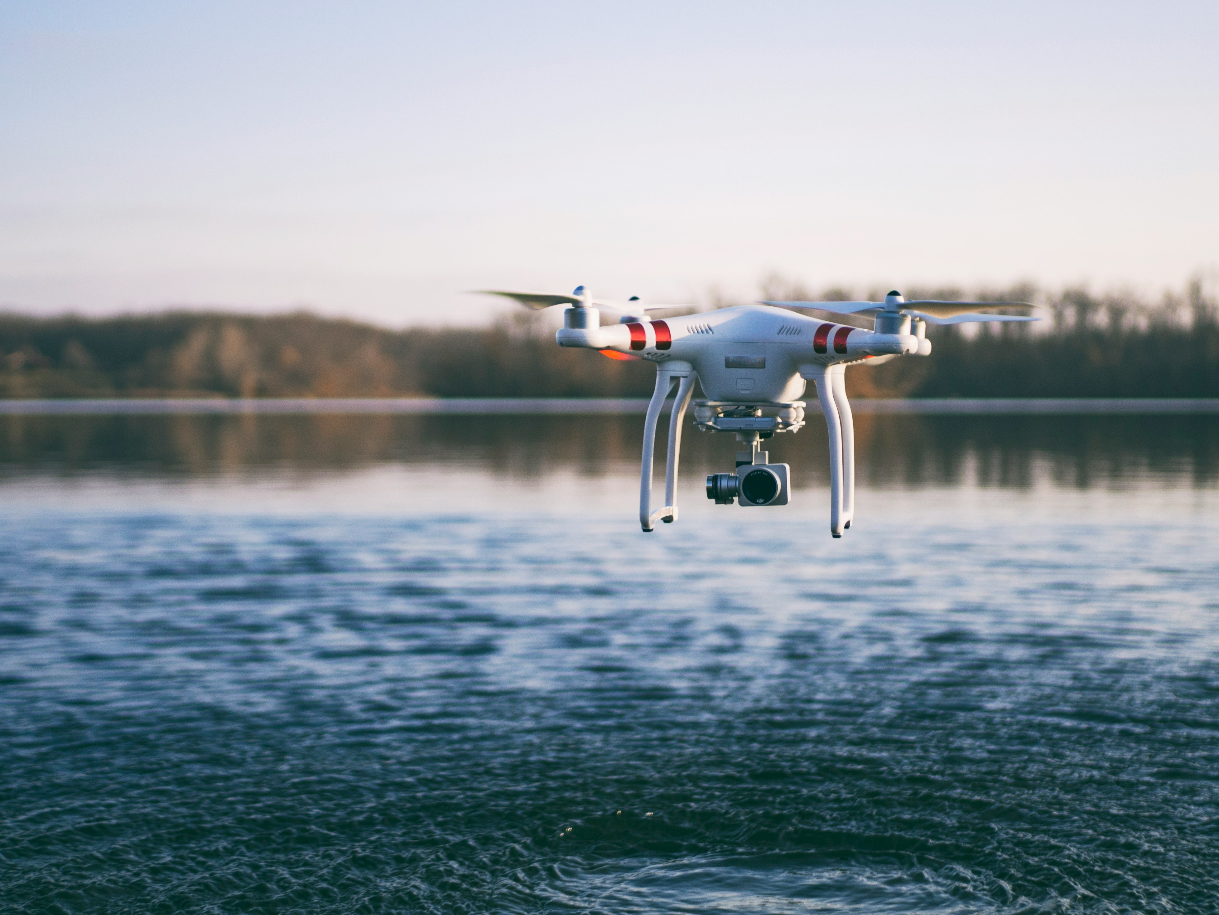 white quadcopter drone flying above body of water